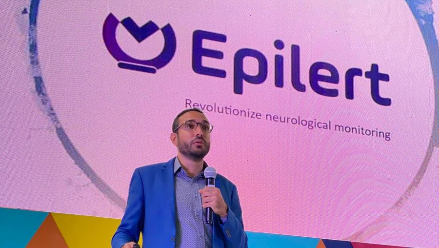 Amine Riahi pitching Epilert on stage at an AfricArena event, with the Epilert logo on the screen behind him